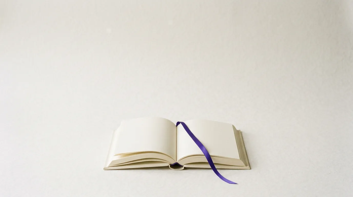 An open book with blank ivory pages and a violet ribbon bookmark.