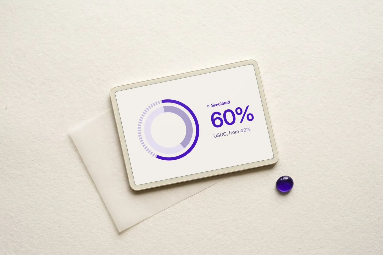 A tablet resting on a sheet of tissue paper beside a violet glass bead. The screen shows a ring chart marked Simulated: 60% USDC, from 42%.